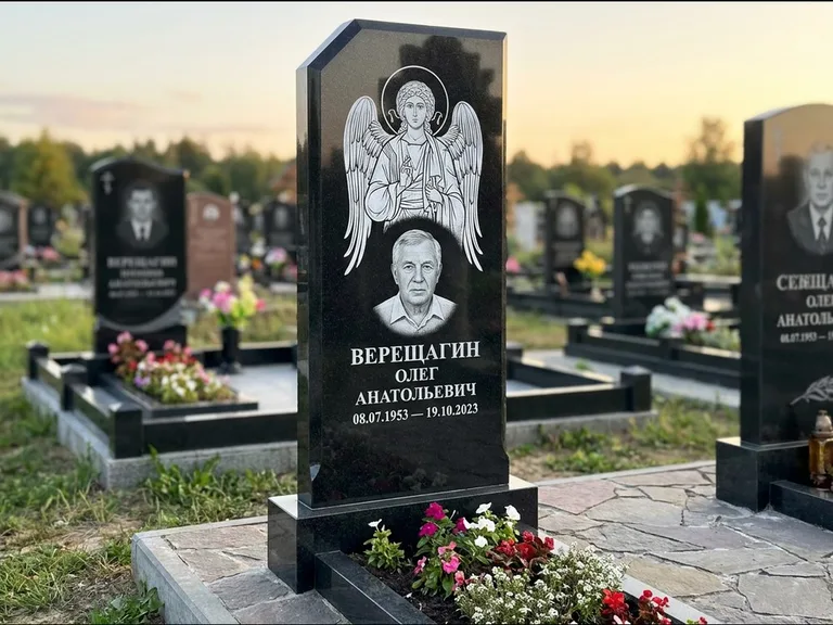 Памятник с гравировкой иконы: стела с резным навершием и нимбом в золоте — гравировка образа Спасителя, высокие разросшиеся туи полукругом, работа «Мельникова» в Новокузнецке