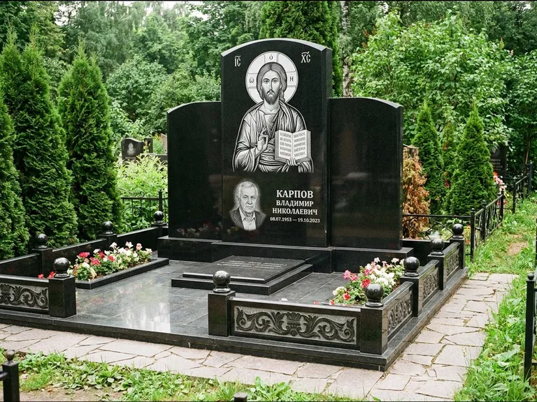 Памятник с гравировкой иконы: широкая панорамная стела с золочёным нимбом — гравировка образа Матроны Московской, цветник с белыми хризантемами, работа «Мельникова» в Новокузнецке