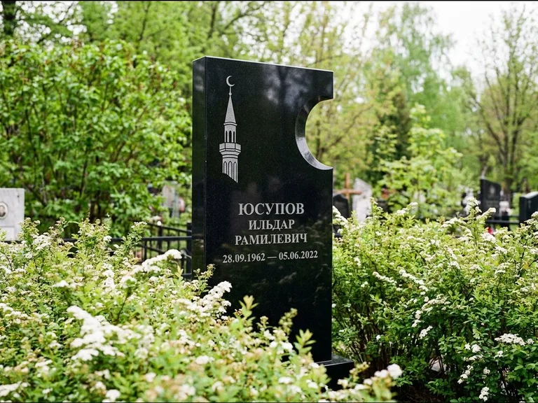 Мусульманский памятник с гравировкой мечети: стела с боковым вырезом в форме полумесяца — гравировка минарета с полумесяцем, низкие кусты спиреи в цвету, работа «Юсупов» в Новокузнецке