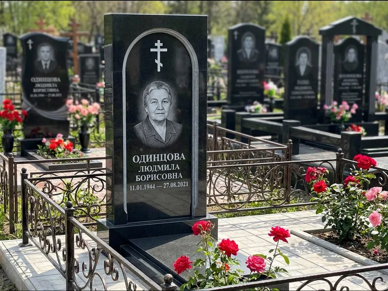 Памятник из чёрного гранита — скромная невысокая стела с крестом с терновым венцом, работа «Лаврентьева» в Новокузнецке